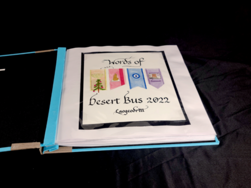 Photograph of the title page of a scrapbook. It contains a large, square white page, with a black inset border (consisting of glued paper), with a painting mounted in the middle. The painting reads, 'Words of Desert Bus 2022 - Laogeodritt' in italic script calligraphy, split in three lines, with four banners in between the lines. The first banner is orange and yellow, portraying a decorated Christmas tree (drawn using Japanese calligraphic strokes), with a seven-branch menorah. The second banner is light red with a dark red vertical stripe, and a croquembouche depicted on it. The text 'for Jacob' is above both of them with arrows pointing to them. The third banner is blue with two dark blue vertical stripes, and a blue-and-white target symbol. The last banner is purple with a dark purple Z on it, and a Zoom window labelled 'CORI' depicting a person with a paper bag over their head.